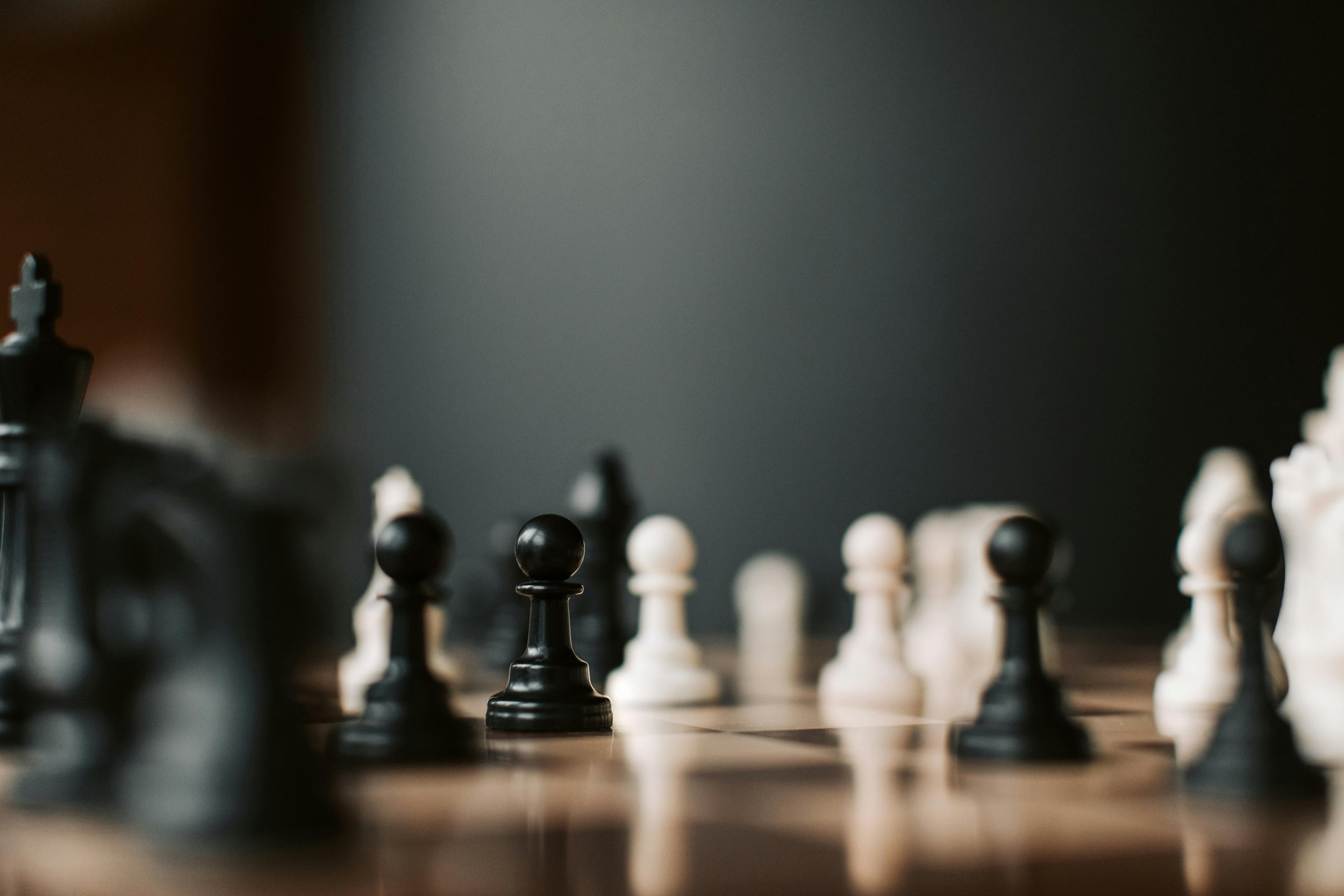 Close-up of black and white chess pieces on a wooden board, with a black pawn in focus.