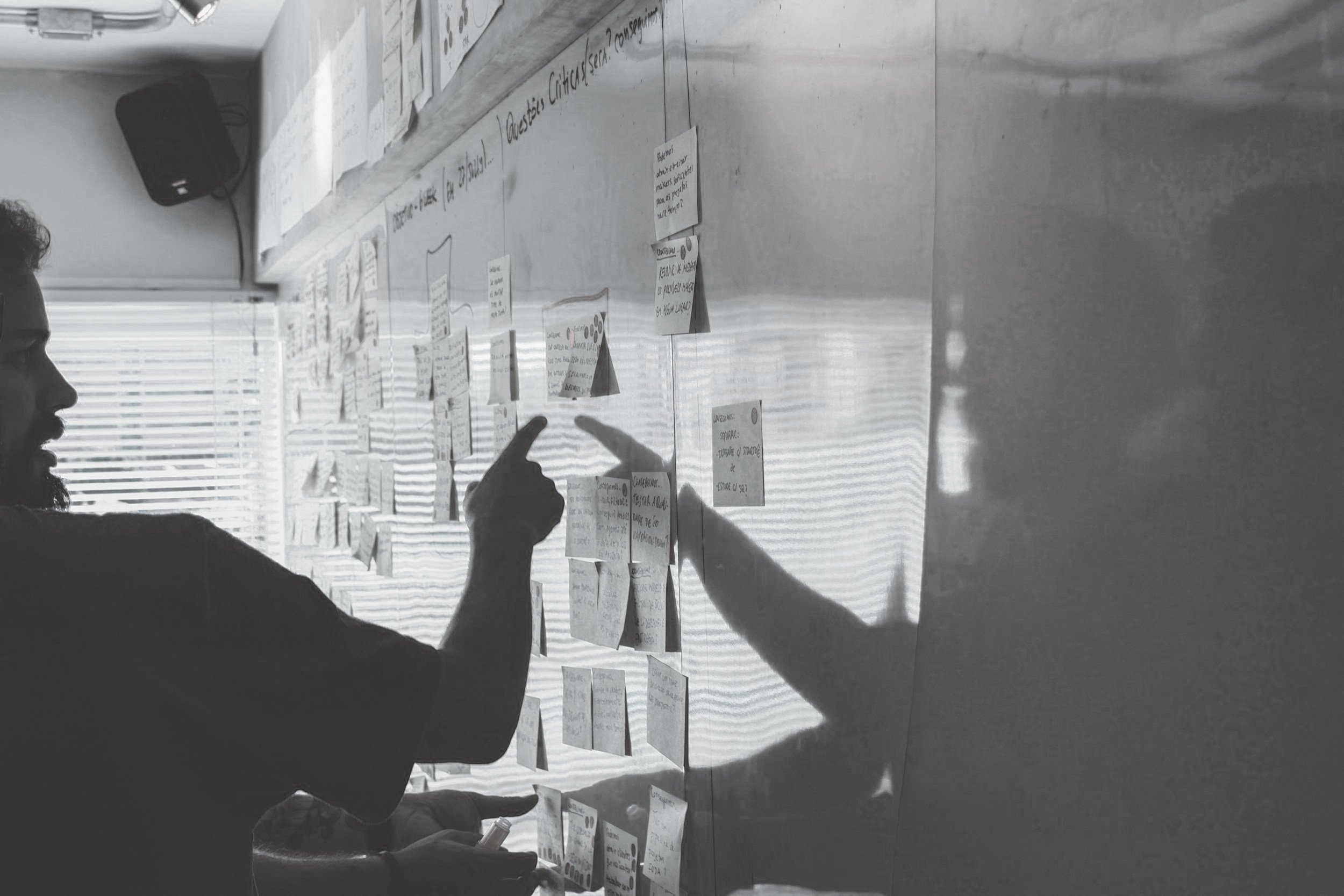 A person pointing at handwritten notes on a glass wall during a planning session.