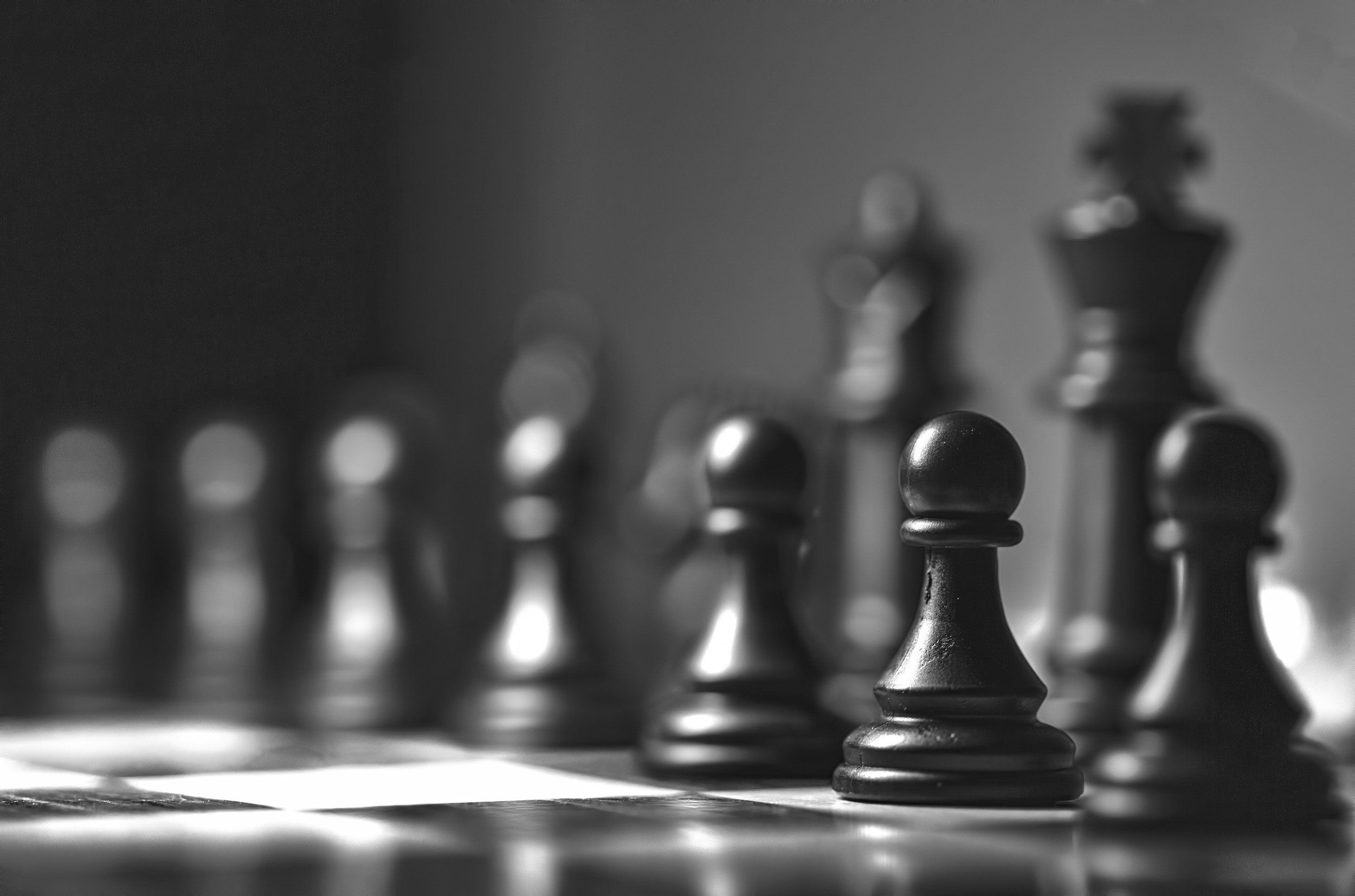 Black and white close-up of chess pieces, with a pawn in the foreground and larger pieces behind it.